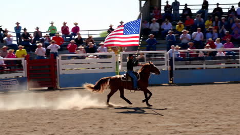 person on horseback carrying american flag in rodeo arena