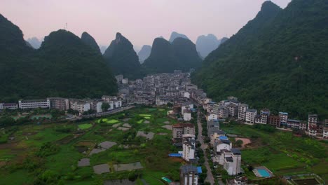 el hiperlapso aéreo captura coches que conducen desde campos de cultivo a la ciudad de yangshuo, enclavada en medio de montañas verdes al amanecer.