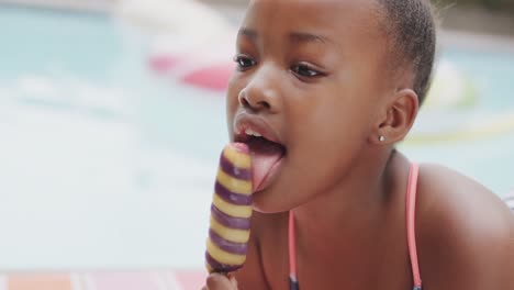 Happy-african-american-girl-smiling-and-eating-ice-cream-by-swimming-pool,-slow-motion,-unaltered