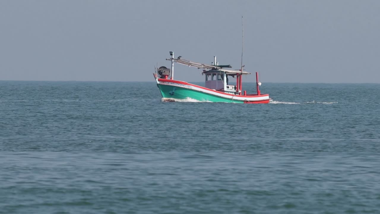 Un colorato peschereccio naviga in acque oceaniche tranquille sotto un cielo sereno e leggermente velato