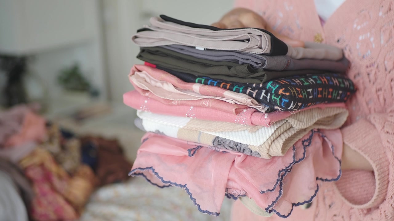 Woman Holding a Stack of Folded Clothes in a Bedroom