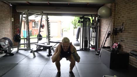 tattooed man in home gym front shot doing squat jumps