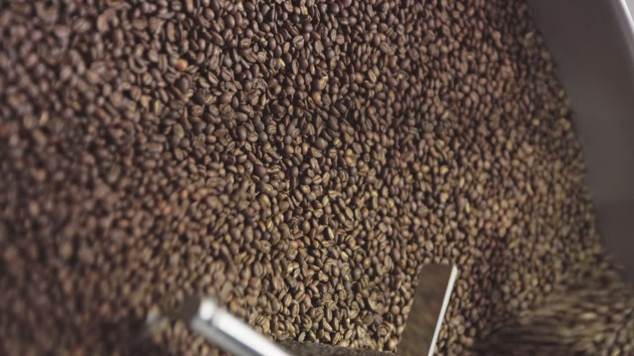 Vertical, closeup of coffee beans tumble roasted in drum machine, slow motion