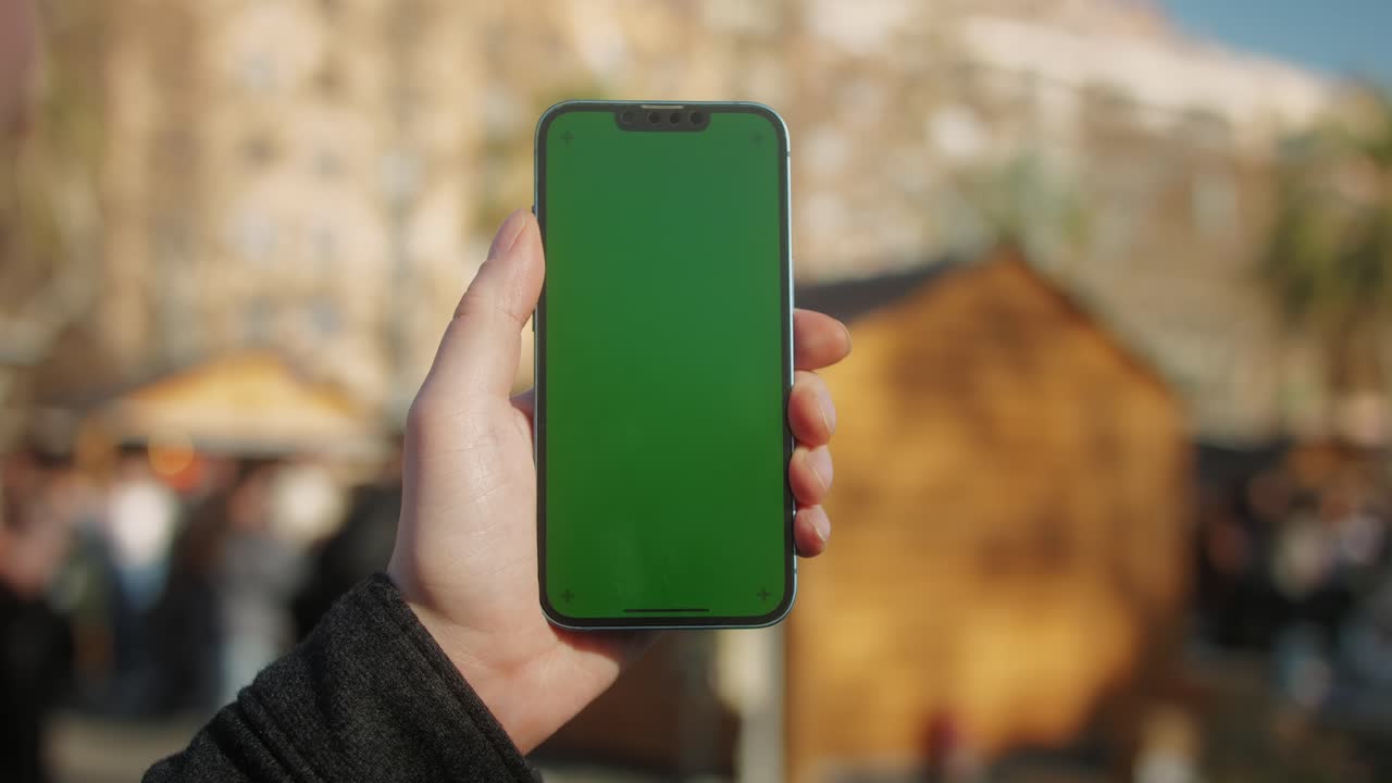 Young man holding phone chroma key screen on the street close-up. Male with green screen on smart phone swiping .