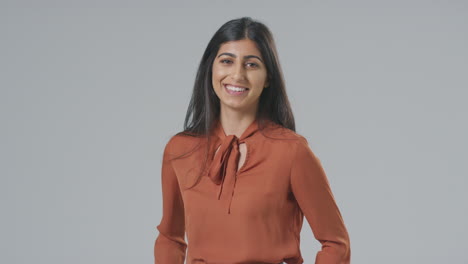 Studio-Portrait-Of-Smiling-Young-Businesswoman-Putting-Hands-In-Pockets-Against-Plain-Background