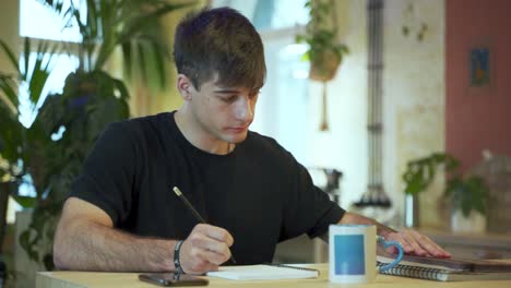 un joven estudiante europeo está haciendo su tarea en la cafetería con antecedentes naturales
