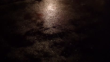 raining dark road lit by a street light at night - camera tilt down