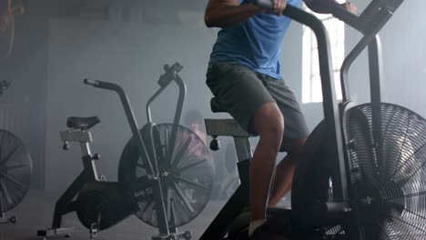 hombre biracial decidido entrenando duro en bicicleta elíptica en el gimnasio, en cámara lenta.