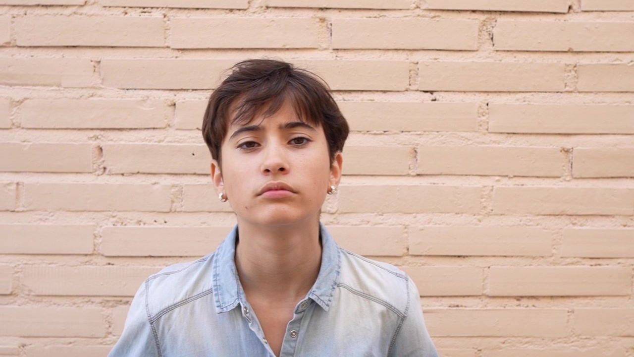 Una donna contemplativa indossa una camicia di jeans ed è in posa su uno sfondo semplice.