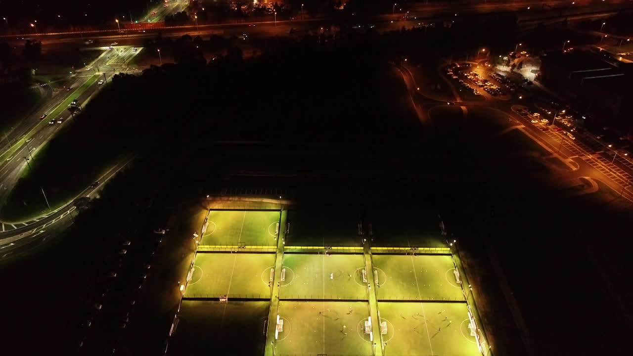 Slow view looking up from football field at night over metropolitan night landscape surrounding.