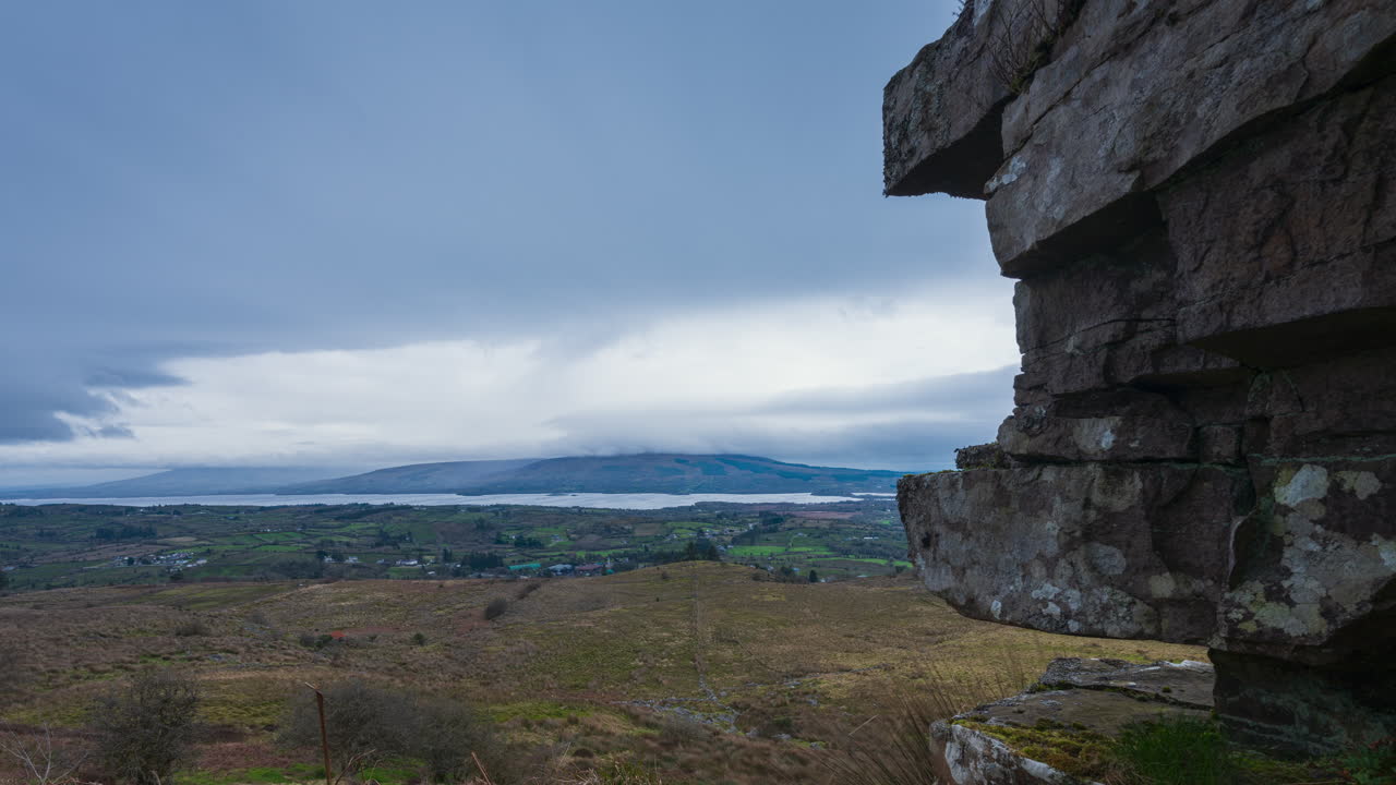 Time lapse of rural landscape with a massive boulder in the foreground and hills and lake in the distance on overcast cloudy day in Arigna mountains in county Leitrim in Ireland