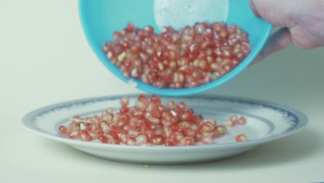 pomegranate seeds pouring out of bowl onto plate