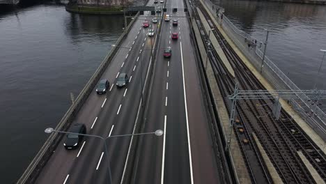 Drone-tilt-down-above-six-lane-highway-crossing-river-by-empty-railroad-tracks-on-cold-winter-day