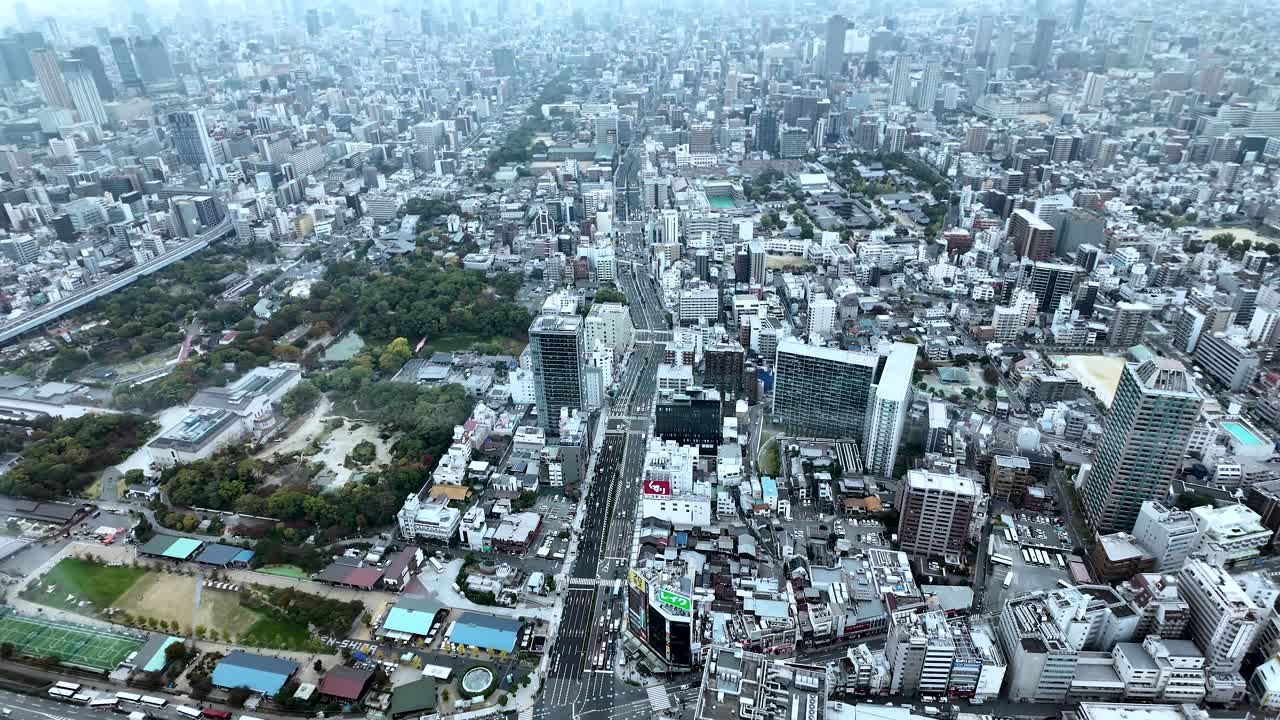 Aerial view of Osaka cityscape featuring a park and skyscrapers on a cloudy day, capturing urban density and green spaces