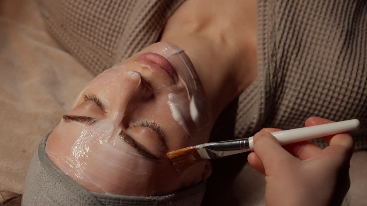 Estetista che applica una maschera viso sul volto di una donna con un pennello