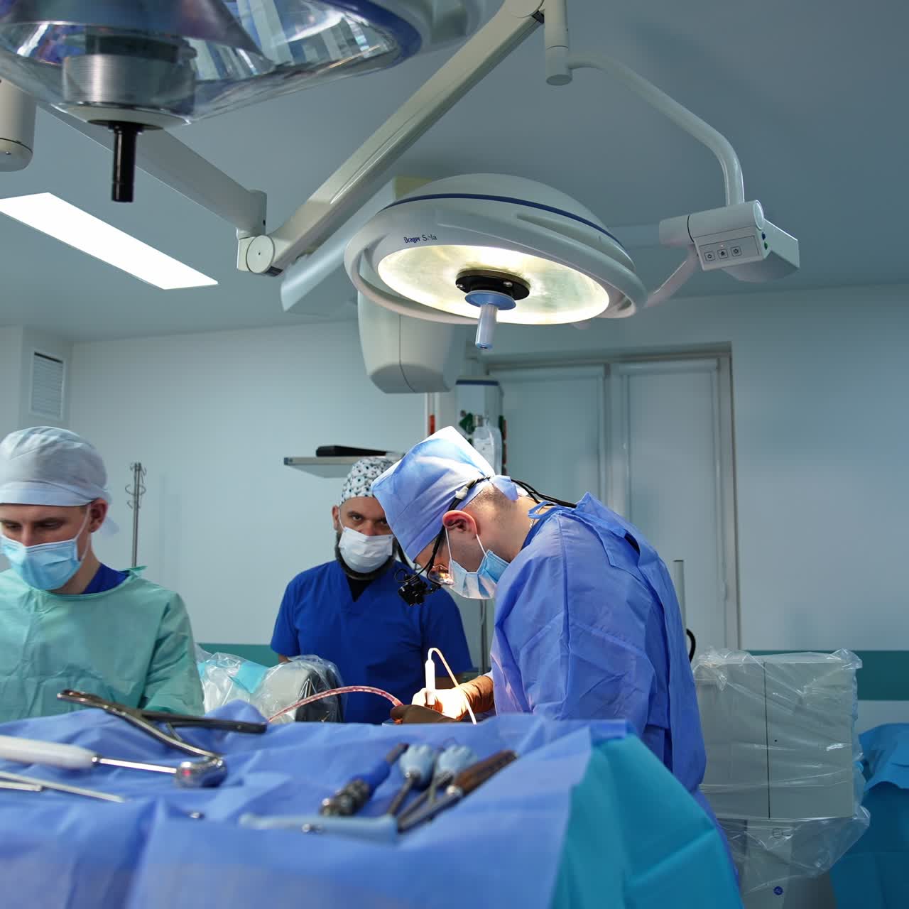 Professional surgeon operating the patient in the middle of modern surgery room. Assistant and anesthesiologist standing beside the doctor
