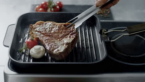 Chef-cooking-steak-at-griddle-pan.-Closeup-man-hands-turning-steak-with-tongs.