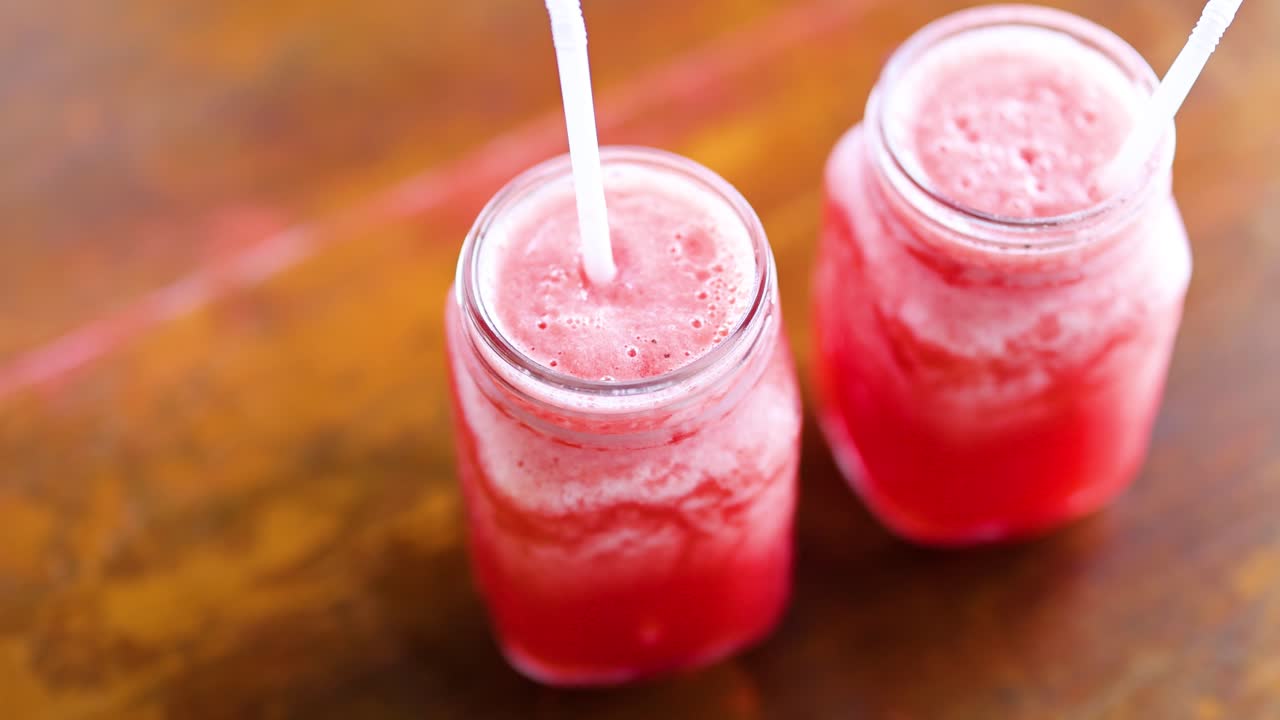 A hand stirs watermelon juice in mason jars on a wooden table, highlighting a refreshing beverage preparation