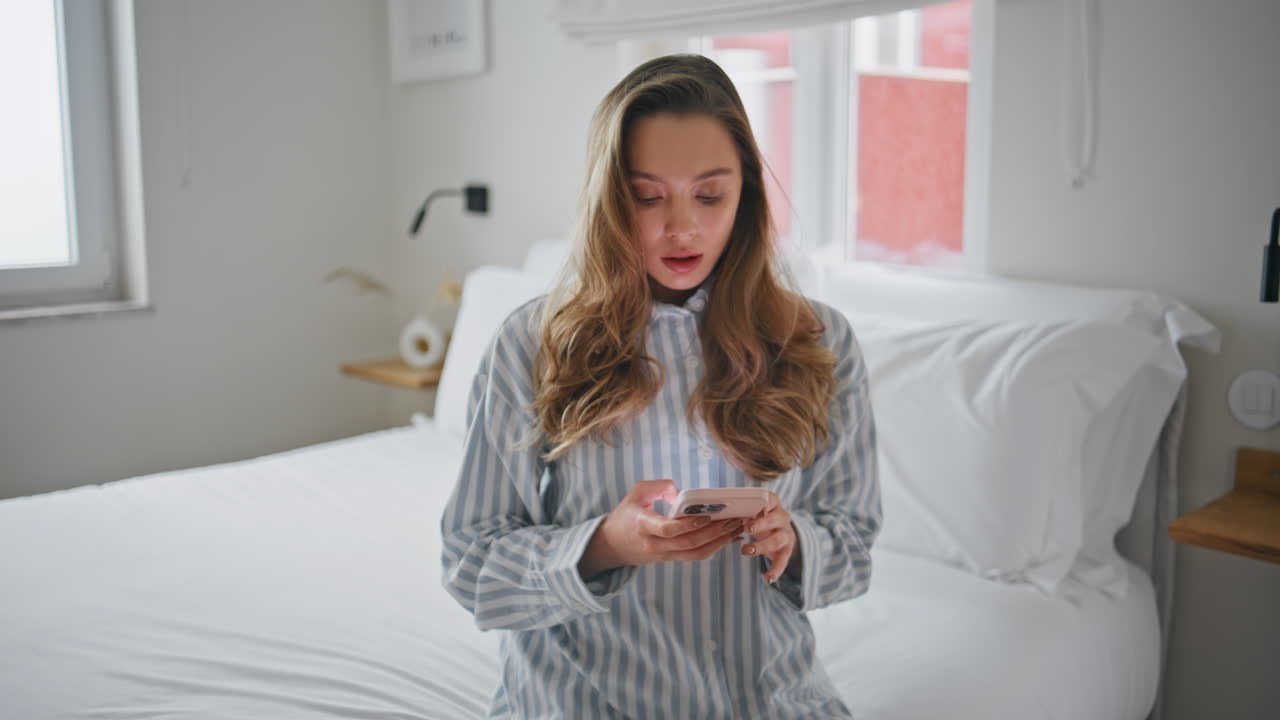Interested girl browsing mobile phone in cozy apartment bedroom closeup