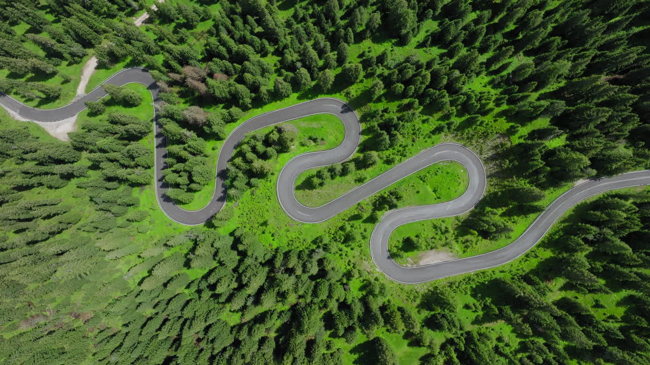 Aerial footage of the serpentine road winding through Giau Pass in the Dolomites during spring, surrounded by lush alpine meadows