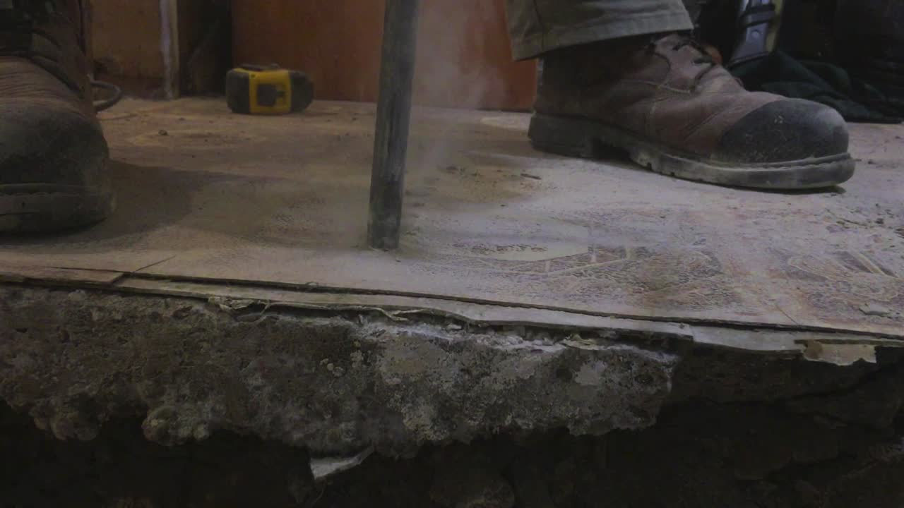 드릴 헤드에서 연기가 피어오르는 콘크리트 철거 드릴 비트와 작업자 부츠를 닫습니다.