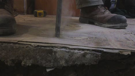primer plano de la broca de demolición de hormigón y las botas de los trabajadores con humo saliendo del cabezal de perforación
