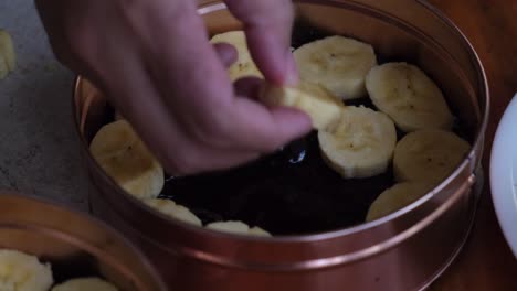 Bäcker,-Der-Scheiben-Reifer-Bananen-Auf-Banoffee-Kuchen-Mischung-In-Einer-Blechdose-Legt