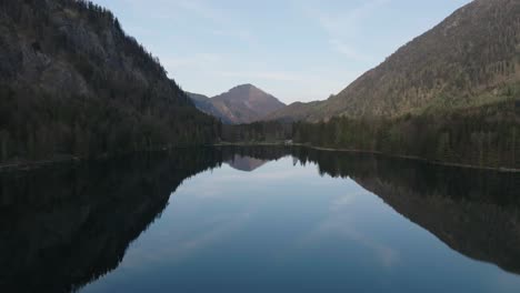 Volando-Sobre-El-Agua-Tranquila-Del-Lago-Con-Reflejo-De-Espejo-De-Las-Colinas-De-Los-Alpes,-Langbathseen,-Alta-Austria