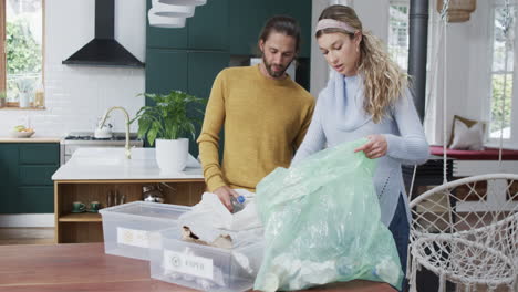 Diverse-couple-segregating-plastic-bottles-and-paper-at-home,-slow-motion