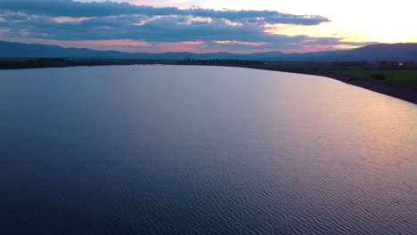 4k cinematic drone stock footage flying over a lake in romania at a beautiful sunset in landscape with silhouette trees and colorful sunset sky