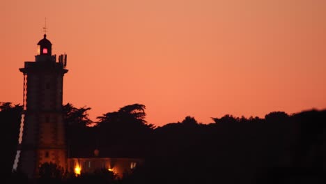 sunset-painting-the-sky-in-several-shades-of-red-with-lighthouse-silhouette,-Cascais,-Portugal