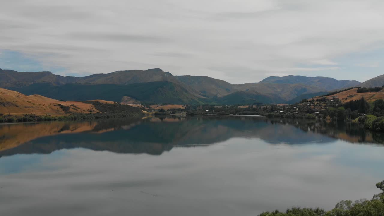 cámara lenta - volando sobre el lago hayes cerca de queenstown, nueva zelanda con montañas en el fondo - antena