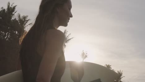 close up view of a young sporty girl walking on a tropical beach with her surfboard