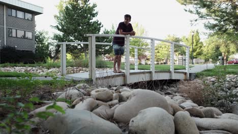 joven caucásico reflexiona sobre la vida mientras está de pie junto a un puente peatonal en un parque público y luego se aleja