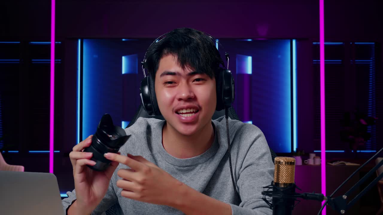 primer plano de un hombre asiático sonriente con una computadora revisando la cámara len en una habitación iluminada por luces de neón en retro