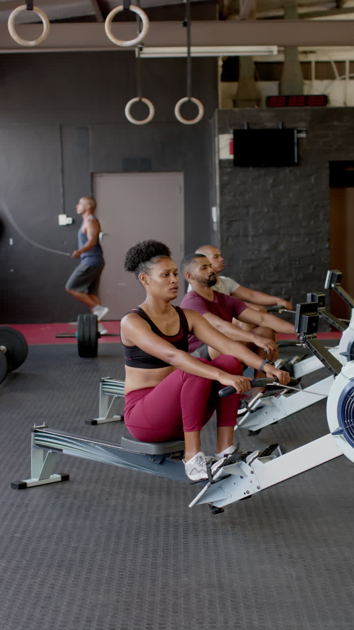 Vertical video of diverse sports people using rowing machines at gym in slow motion