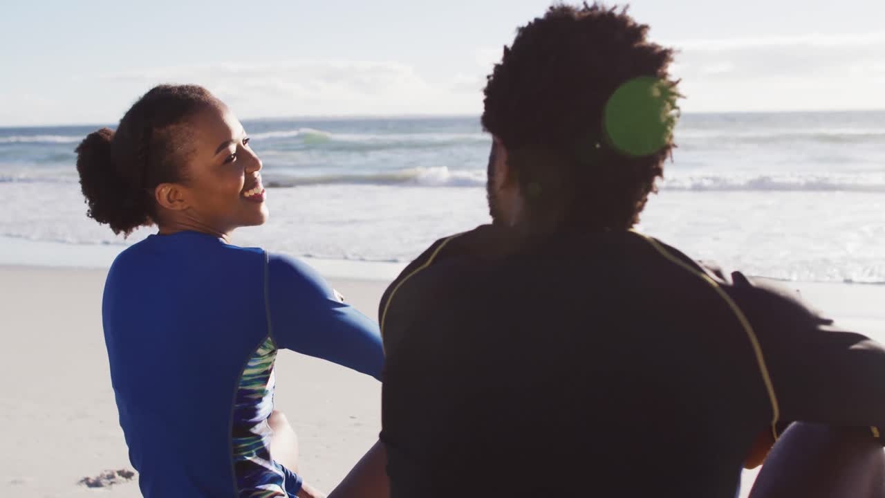 African american couple talking and sitting on the beach