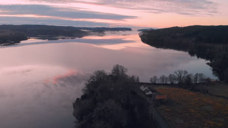 aerial view of a pink sunset sky reflecting into a calm lake, wide shot, drone flying forward