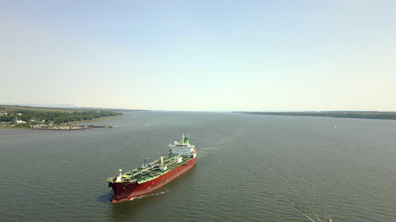 In this drone video, as you glide above the river, you'll be drawn towards a magnificent red cargo ship cruising gracefully, a testament to the bustling maritime activity of the region