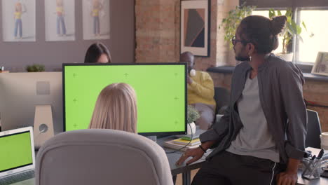 two multiethnic colleagues looking at monitor with green screen and discussing new project in an animation studio