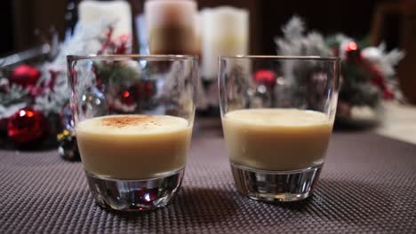 dos vasos de ponche de huevo navideño con canela molida añadida adornada con adornos navideños