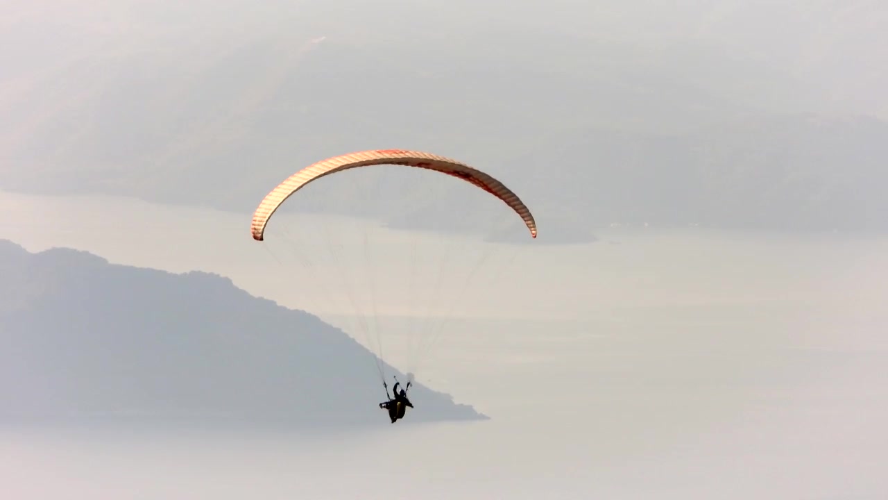 Paraglider svever over naturskjønt fjellandskap og innsjø