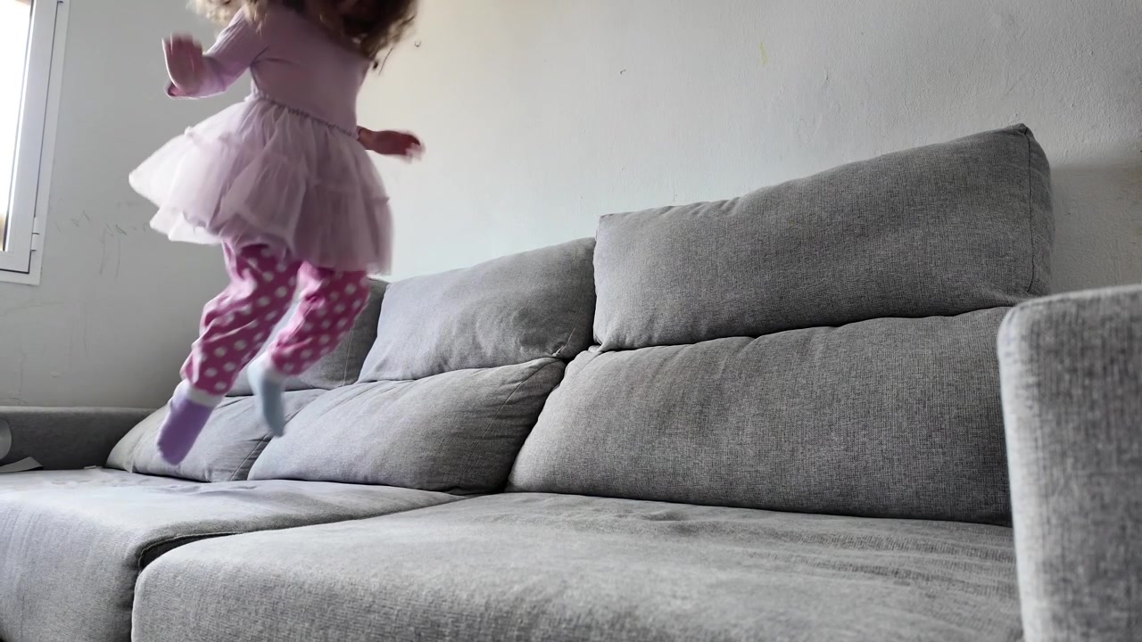 Lille pige hopper på sofaen i slowmotion derhjemme, et legende barndomsøjeblik