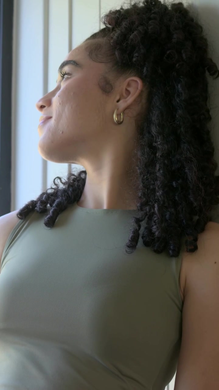 Video verticale: Donna adulta che si sistema, controlla il telefono vicino alla finestra, tiene una tazza, indossa un top color oliva