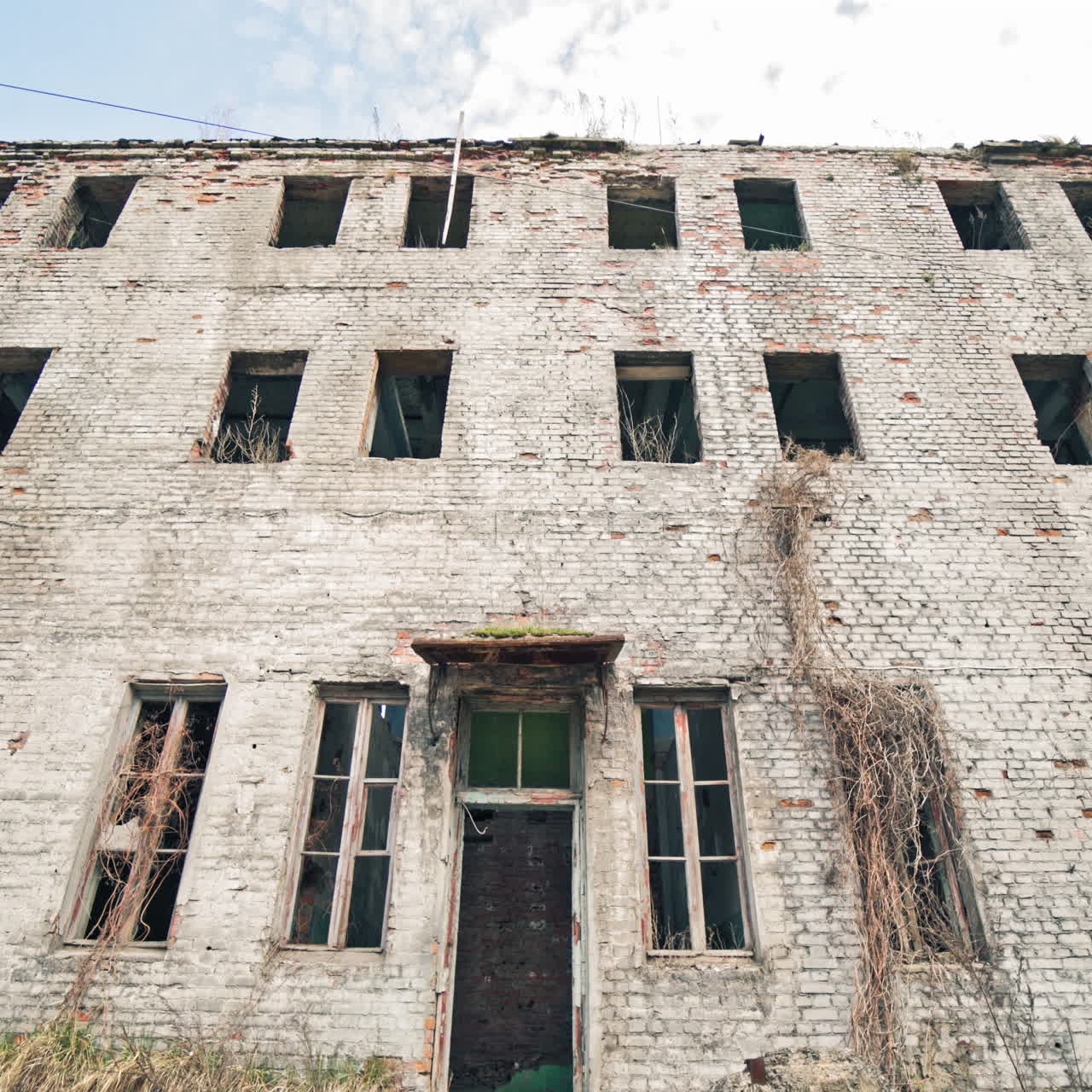 Abandoned building with broken windows in the war. Damaged brick three-storeyed building outside. Camera moves back.