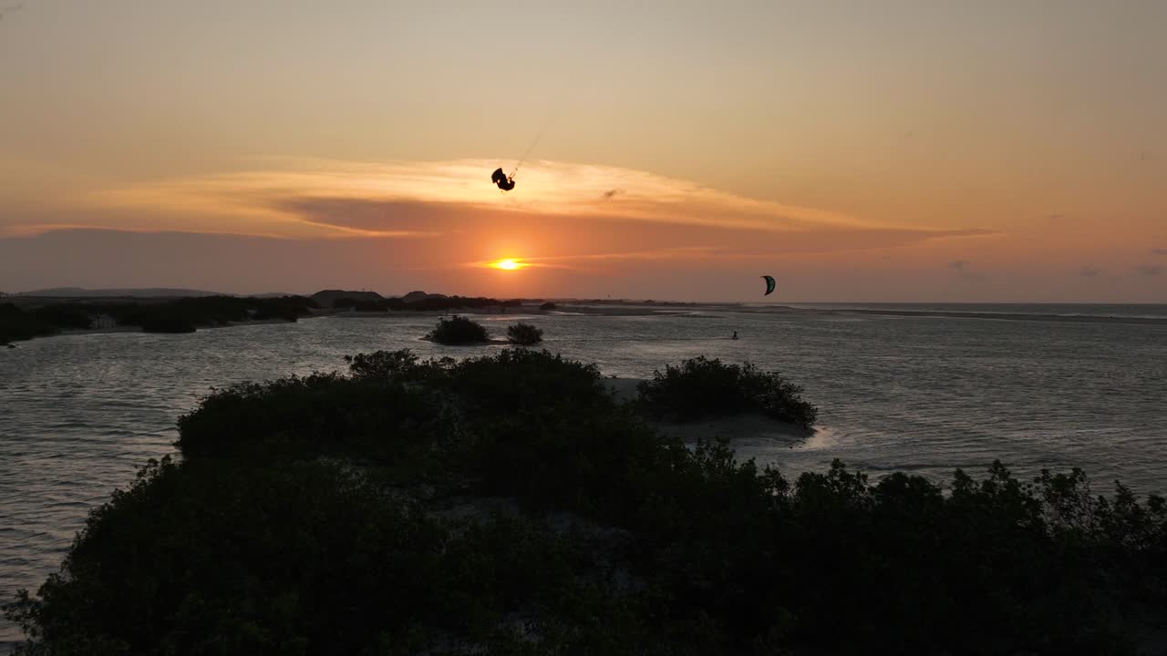 kitesurfer hacer un gran salto sobre el banco de arena - siluetas contra el cielo dorado del atardecer