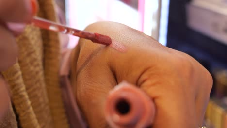 woman applying pink lipstick to her hand