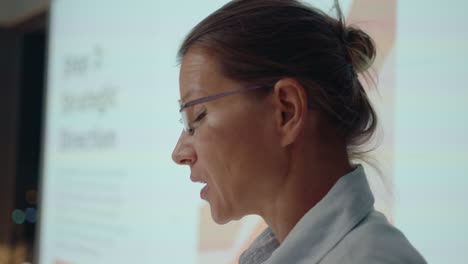 woman standing by projection screen and giving business presentation during corporate meeting late in the office. medium close-up shot, focus on foreground