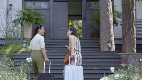 happy asian female friends with suitcases walking on stairs of home on sunny day, slow motion