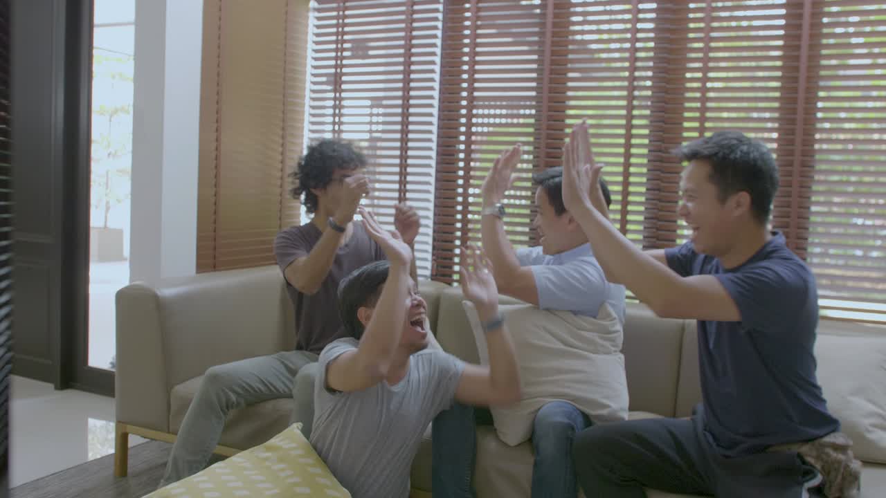 아시안 메이트 그룹이 집에서 tv에서 스포츠 대회를 보고 있습니다.